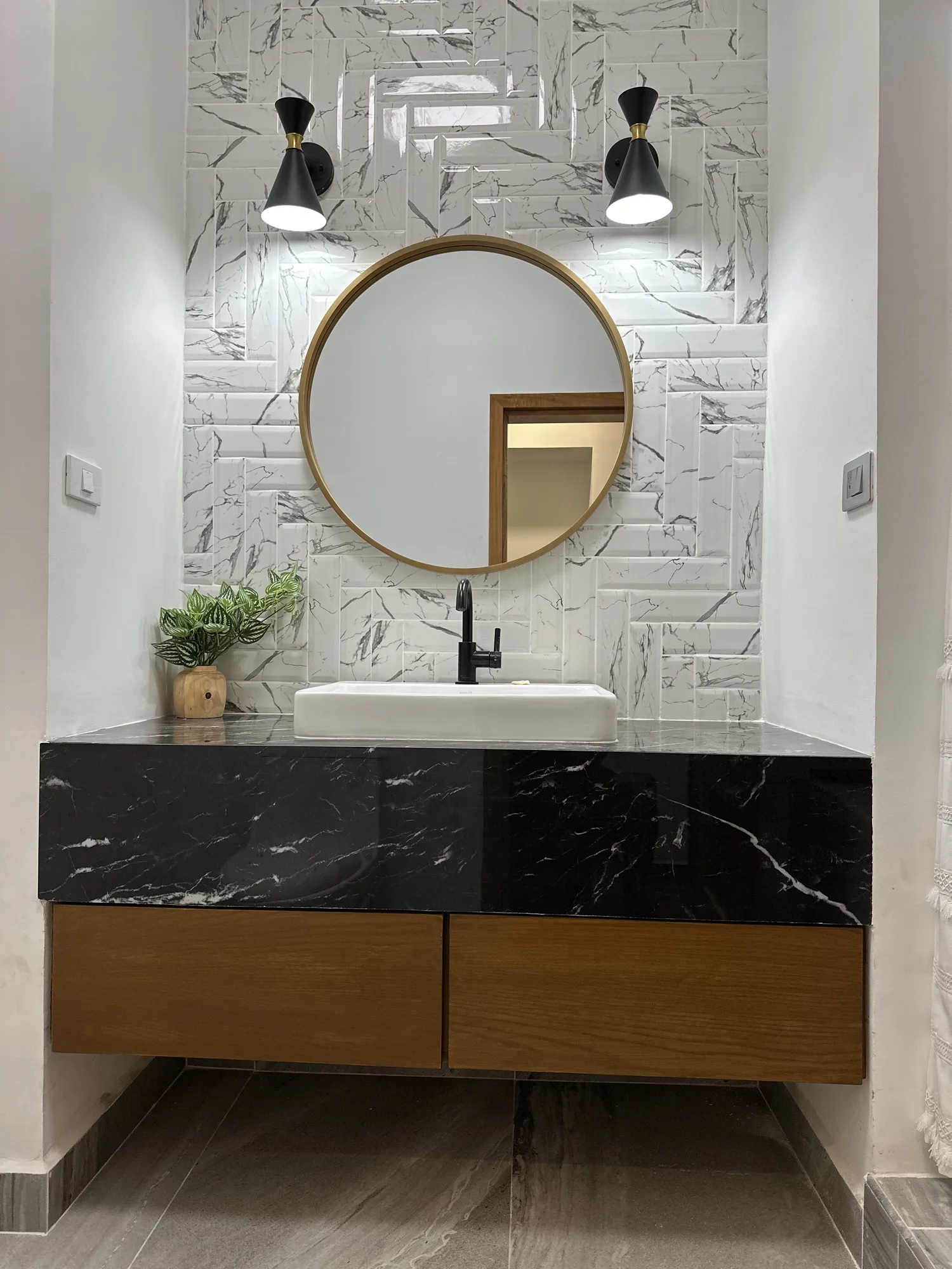 Mueble de baño flotante con cubierta de mármol negro, cajones de madera y espejo circular de latón