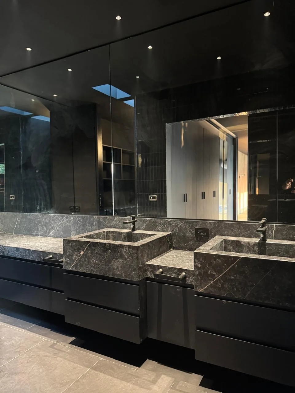 Baño negro con doble lavabo de mármol gris labrado en bloque y cajones flotantes en negro mate