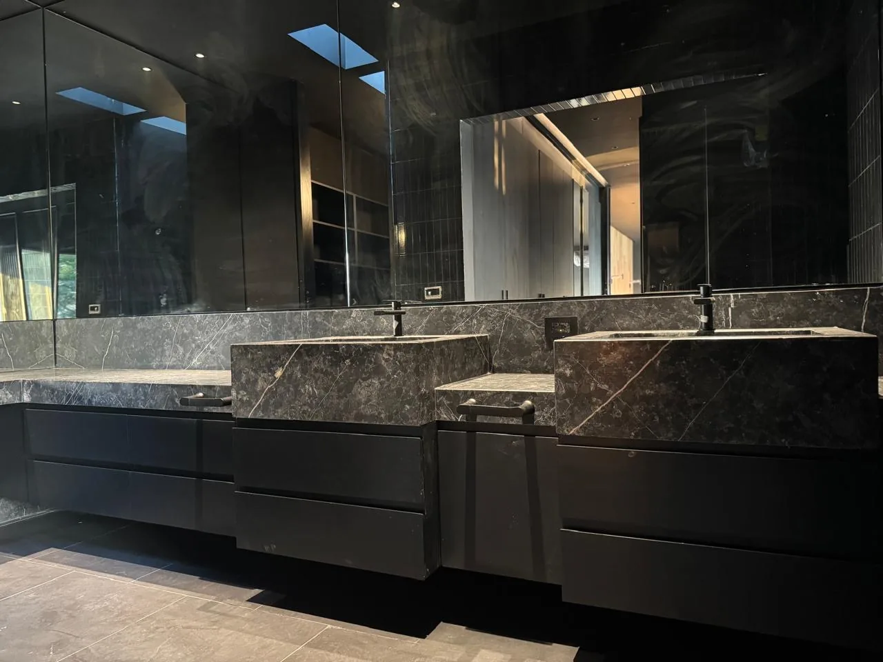 Baño monocromático en negro con doble lavabo de mármol gris labrado en bloque y mobiliario flotante negro mate