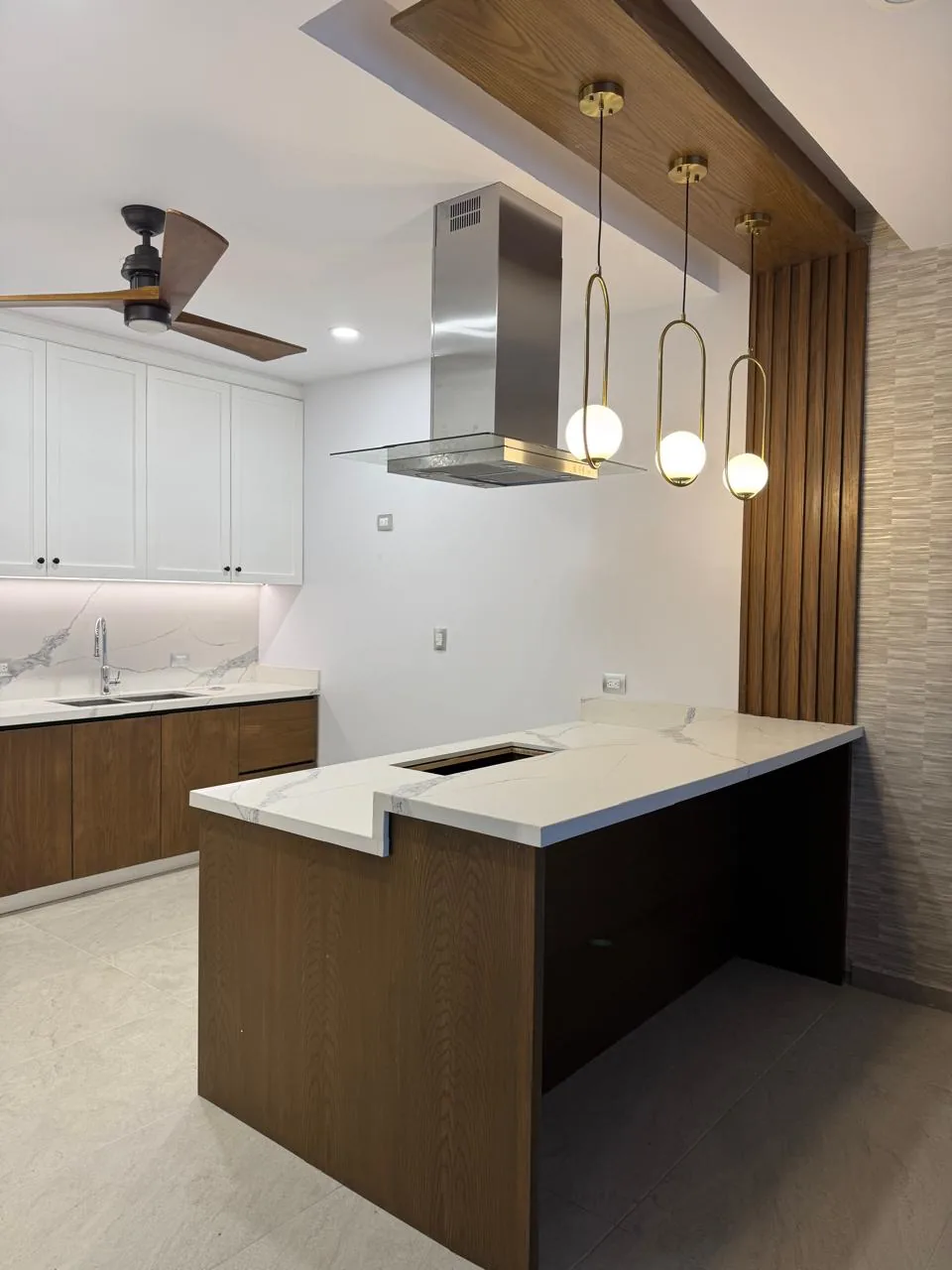 Cocina con isla de nogal y cubierta de cuarzo blanco, plafón de madera con lámparas colgantes de latón y celosía de listones