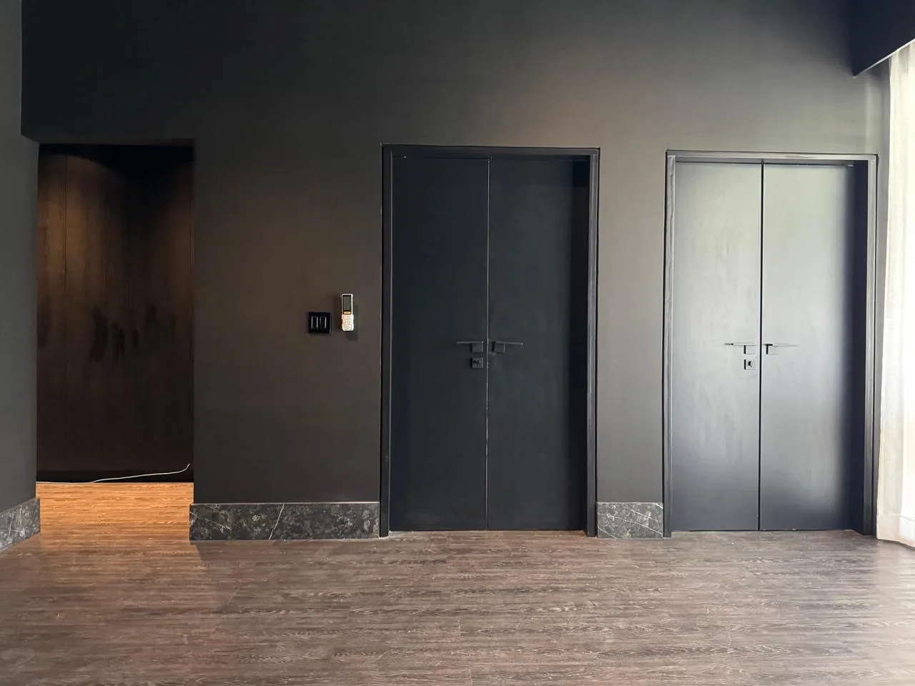 Puertas dobles de madera en negro mate que integran el elevador al muro, con zoclo de mármol y piso de madera