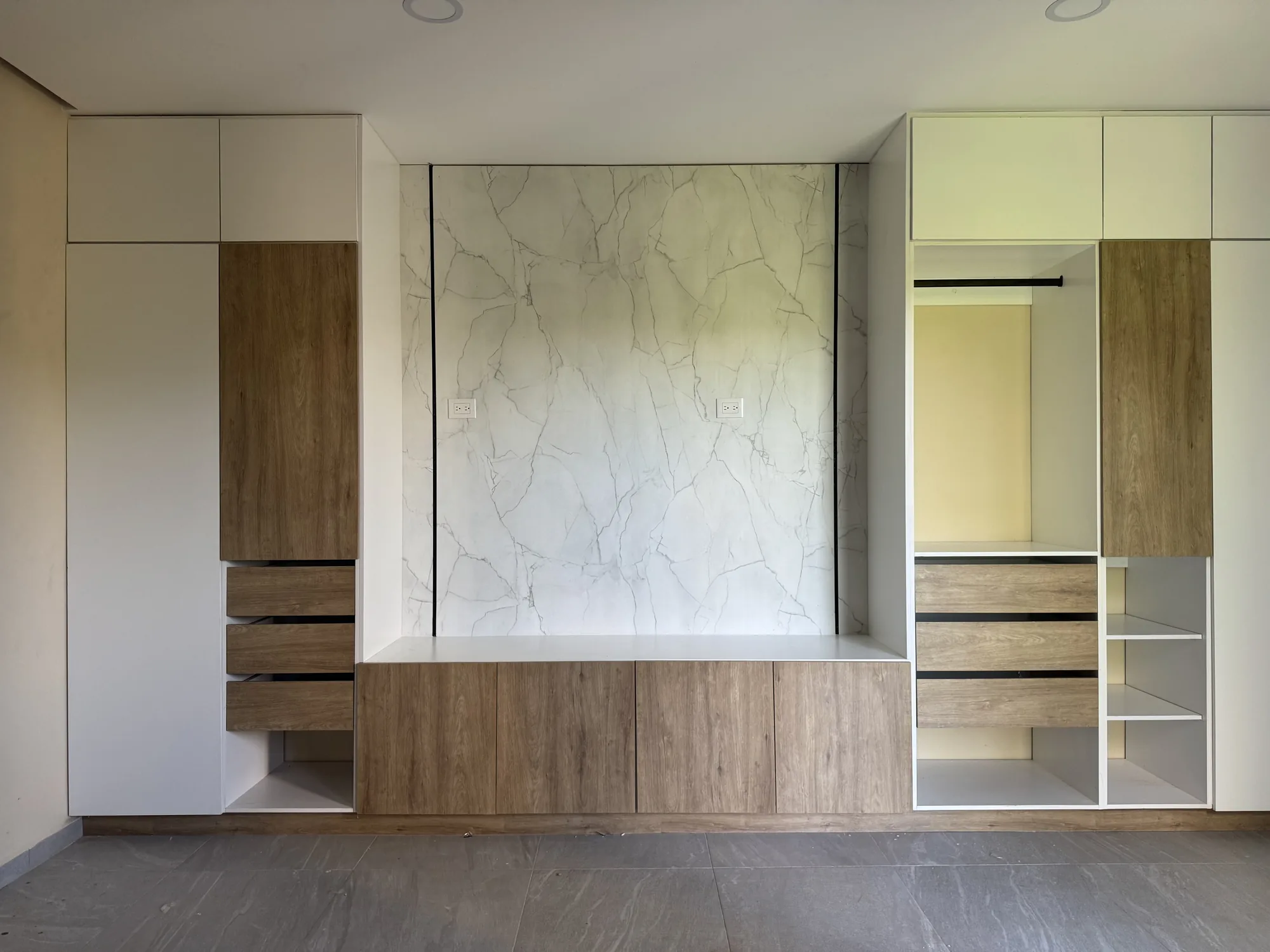Recámara con muro de mármol blanco, vestidor abierto y mueble bajo de madera clara hecho a la medida
